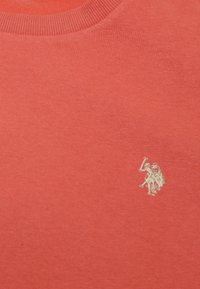 Czerwony bawełniany sweter z okrągłym ściągaczem. Zawiera małe haftowane logo w złotym kolorze po lewej stronie. Gładka tekstura, casualowy design.