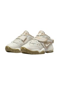 Nike-skor med ett ljust beige syntetiskt överdel, texturerade detaljer, justerbart rem och en gummisula med en något genomskinlig brun nyans.