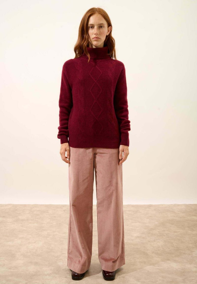 Suéter de cuello alto burdeos con patrón de diamantes, combinado con pantalones de pierna ancha rosas. Ambas prendas tienen texturas suaves y un ajuste relajado.