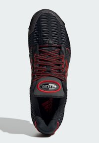 Black athletic shoe with red accents, mesh upper, textured design, and contrasting rubber sole. Features red laces and padded collar.