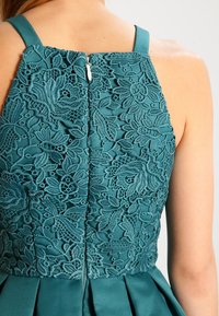 Tealfärgad klänning med en spetsbyxa med intrikata blommönster, en figurnära midja och en dold dragkedja bak.