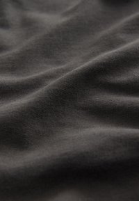 Gros plan sur un tissu doux de couleur gris foncé montrant une texture fine en maille et des plis naturels avec des ombres douces.