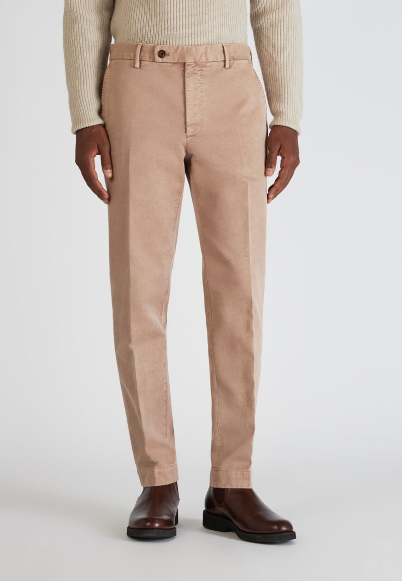 Helle rosa Chinos mit geradem Schnitt, aus Baumwollstoff und mit einem Knopfverschluss vorne. Kombiniert mit braunen Stiefeletten.