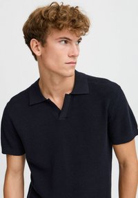 Navy short-sleeve polo shirt made from textured fabric, featuring a partial button placket and a flat collar design.
