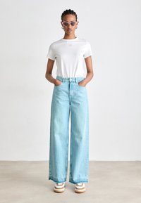 Lyseblå vide jeans med høyt liv, sammen med en hvit t-skjorte med et lite rosa hjerte-design, og retro-stil rosa solbriller.