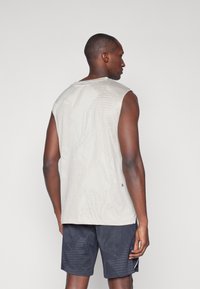 Muscle-Tanktop in hellem Beige mit strukturierten, geometrischen Mustern; ärmelloses Design. Kombiniert mit dunkel gemusterten Shorts, die einen Kontrast im Stil zeigen.