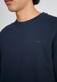 Sudadera de color azul marino fabricada en suave algodón, con un cuello redondo y un pequeño logo en relieve en el pecho. Diseño minimalista.