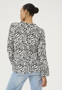 Black and white patterned blouse with long sleeves, lightweight fabric, open back, and gathered details, paired with light blue jeans.
