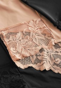 Spetspanel i peachfärg med blommönster, lager på svart tyg. Den släta texturen av spets kontrasterar med det ogenomskinliga svarta materialet.