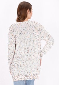 Pulover tricotat în alb, cu stropi multicolori, având o croială lejeră, mâneci lungi și un tiv rotunjit, prezentând un model texturat.