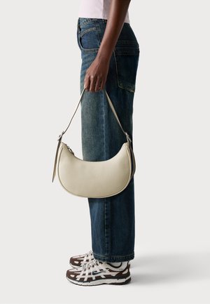 Cremfarbene Leder-Schultertasche mit geschwungener Form und strukturiertem Oberflächenmaterial, ausgestattet mit einem langen Tragegurt und silbernen Hardwareakzenten.