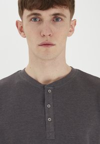 Cămașă henley gri dintr-un material texturat, cu un guler rotund și placket cu trei nasturi. Design simplu, casual, fără modele sau accente.