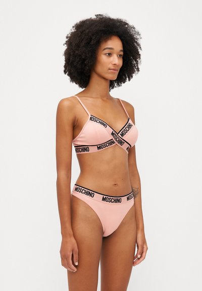 Gaiši rozā bikini komplekts, kurā ir bralete ar plānām siksniņām un V formas dizainu, papildināts ar atbilstošiem stringiem ar melnu logotipa jostu.