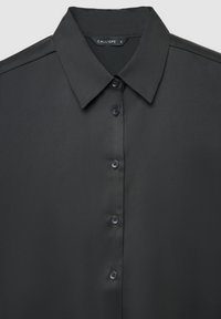 Schwarzes, glattes Stoffhemd mit spitzem Kragen und fünf schwarzen Knöpfen vorne, etikettiert mit "Calliope", Größe klein.