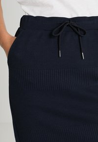 Jupe côtelée marine en matière texturée, dotée d'une taille élastique avec un cordon de serrage aux extrémités métalliques.
