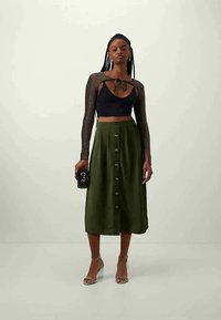 Black crop top with tie detail, green midi skirt with front buttons, clear heels, and a black clutch. Smooth fabric and fitted design.