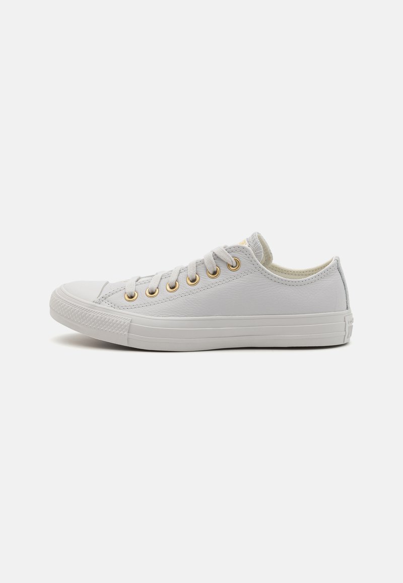 Sneaker bianche basse con tomaia in pelle texture, occhielli dorati e suola in gomma. Presentano una punta arrotondata e un design minimalista.