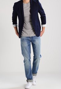 Navy blazer with rolled sleeves, gray T-shirt, light blue jeans, and white sneakers. Denim features a faded wash and subtle wear.