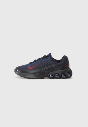 Fekete és tengerészkék sneaker hálós felsőrésszel, piros logóval és jellegzetes párnázott talppal, amely lekerekített részletekkel rendelkezik. Fűzők és párnázott bokréta tartozik hozzá.