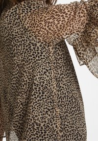 Leopardmönstrad blus med genomskinliga ärmar, med en beige bakgrund och svarta-bruna fläckar. Lätt tyg med flödande, lös design.