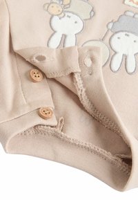 Beige cotton onesie with embroidered animal design. Features wooden buttons at the neck, soft texture, and stitched hem details.