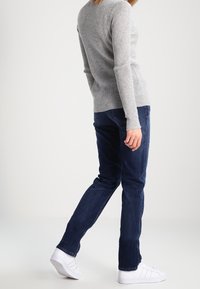 Grå, ribbad långärmad tröja i kombination med mörkblå jeans och vita sneakers. Jeans har en rak passform, och tröjan har en rund halsringning.