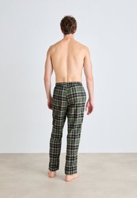 Gröna rutiga byxor med elastisk midja, rak bendesign och medeltjockt bomullstyg, visade bakifrån.
