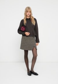 Camisa negra de botones, falda corta de pata de gallo, medias transparentes, bailarinas negras y un clutch burdeos. Presenta un diseño de peplum estructurado.