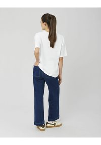 T-shirt blanc surdimensionné, jean en denim foncé à jambes larges et baskets beige avec des accents bruns, vus de dos.