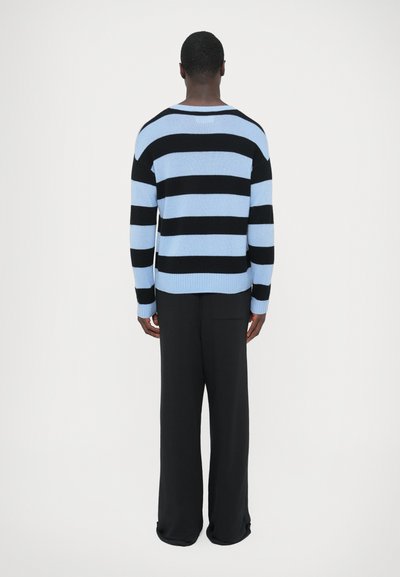 Pull en maille à larges rayures horizontales noires et bleu clair, col rond, poignets et ourlet côtelés, associé à un pantalon noir à jambes larges.