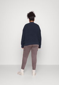 Navyblauer Strickpullover mit lockerem Schnitt, kombiniert mit taupefarbenen Cargo-Hosen mit Seitentaschen und hellbeigen Slippern.
