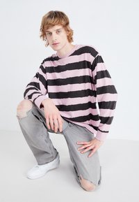Camisa de manga larga a rayas en rosa y negro, hecha de tela suave, combinada con jeans desgastados de color gris claro y zapatillas blancas.