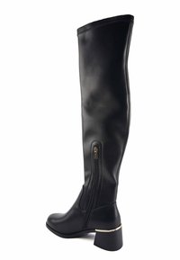 Botas negras por encima de la rodilla, hechas de cuero suave, con cremallera lateral y un tacón grueso con detalles dorados. Diseño recto y ajustado.