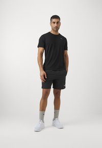Svart treningstrøye og shorts laget av lett stoff, kombinert med grå sokker og hvite joggesko, med en subtil logodetalj.