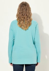 Türkises Langarmshirt aus weichem Stoff, mit Rundhalsausschnitt und lockerer Passform. Getragen mit dunklen Jeans.