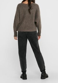 Pull en maille marron à coupe ample et épaules tombantes, associé à un jean taille haute gris foncé et des bottines noires.