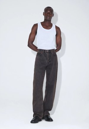 Mørkebrune, vidde jeans med høj talje, kombineret med en hvid ribbet tanktop. Sorte læder sko fuldender outfittet.