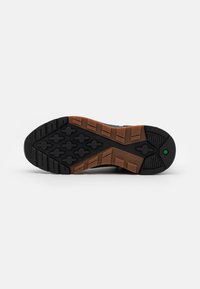 Czarna gumowa podeszwa buta z teksturowanymi rowkami i brązowym śródpodstawem. Zawiera logo Timberland oraz zielony akcent w pobliżu pięty.