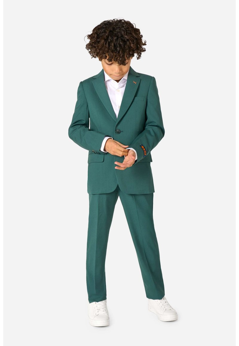 Completo verde a due pezzi per bambini con vestibilità su misura, chiusura con un solo bottone e polsini a contrasto con motivo. Indossato con camicia bianca e scarpe.