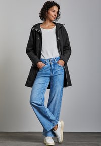 Czarna wodoodporna kurtka z kapturem, biała koszulka, jasnoniebieskie dżinsy o szerokim kroju i białe trampki. Gładki materiał, luźny fason, casualowy design.