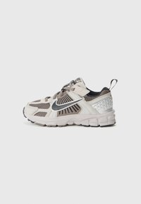 Leichte Sportschuhe in Beige und Grau, mit Netzpaneelen, einem silbernen Nike-Swoosh und einer strukturierten Ferse mit geometrischen Akzenten.