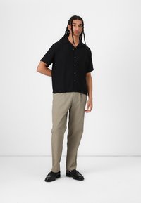 Svart kortermet skjorte med krage, kombinert med teksturerte beige bukser og svarte dressko. Enkelt og skreddersydd design.