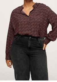 Blouse à manches longues rouge foncé avec petits motifs en forme de cœur rose, dotée d'un col et de boutons, associée à un jean noir taille haute.