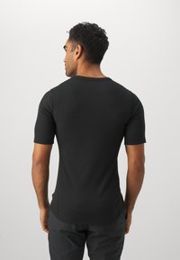 Chemisette noire à manches courtes avec un col rond et une coupe ajustée, fabriquée dans un tissu lisse et extensible, avec des détails de couture discrets.