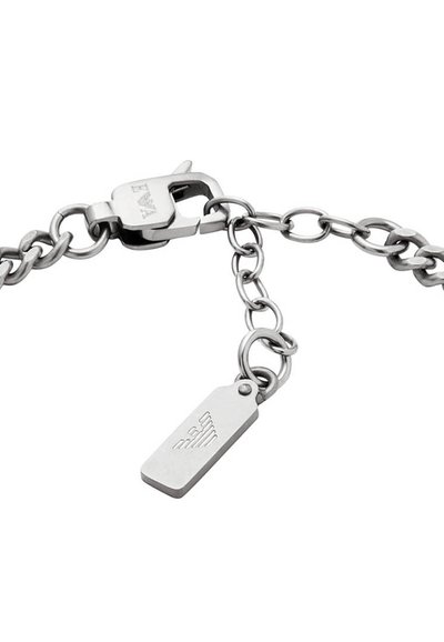Bracelet en chaîne en métal argenté présentant un fermoir à ressort, une petite étiquette avec des détails gravés et des maillons de tailles variées.
