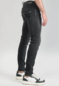 Jeans de denim negro ajustados, con sutil textura desgastada y costuras en contraste, que cuentan con bolsillos traseros y un detalle de cinturón.