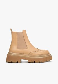 Beżowe skórzane botki typu chelsea z elastycznymi wstawkami, detalami brogue i grubą, teksturowaną gumową podeszwą. Minimalistyczny design i smukły kształt.
