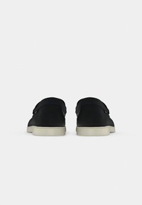 Zwarte suède schoenen met een gladde textuur, een laag profiel ontwerp en witte rubberen zolen. Voorzien van een klittenbandsluiting voor een veilige pasvorm.