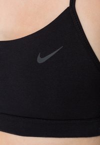 Sujetador deportivo negro hecho de un tejido suave con tirantes ajustables. Presenta un logo gris de Nike de un lado y una banda suave y elástica para mayor soporte.