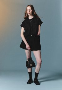Juodas trumpas rankovėmis marškinėliai, derinami su juoda plisėta mini sijonė. Aksesuarai apima mažą juodą krepšį ir iki kelių siekiančias kojines su loafers.